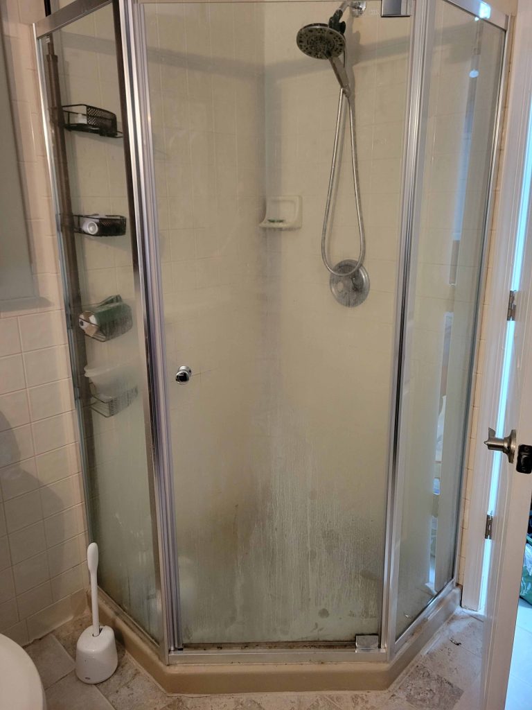 Shower enclosure before deep cleaning, with soap scum on the glass